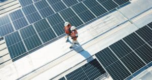 Construction workers in safety equipment inspecting rooftop solar panels